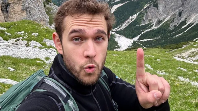 Zedd apuntando con el dedo hacia arriba en una selfie frente a las montañas.